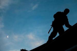 Auftragnehmer in Silhouette, der auf einem Dach arbeitet foto
