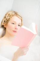 junge Frau entspannt sich und liest ein Buch in der Badewanne foto