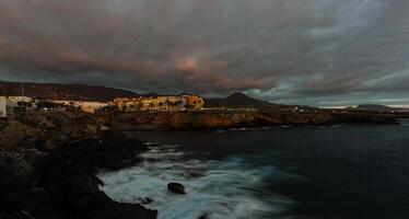 Panorama- Aussicht von das beleuchtet las Amerika beim Nacht gegen das bunt Sonnenuntergang Himmel mit Beleuchtung auf das Horizont auf Tenerife Insel, Spanien foto