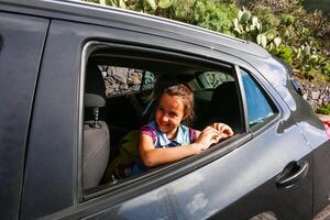 wenig Spaß Mädchen Geschwindigkeiten im Auto in der Nähe von das öffnen Fenster foto