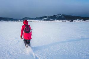 Frau, die an einem kalten Wintertag einsam auf einem zugefrorenen See spaziert foto