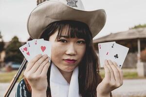 Porträt von ein schön Chinesisch weiblich Cowgirl spielen mit Poker Karten foto