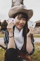 Porträt von ein schön Chinesisch weiblich Cowgirl spielen mit Poker Karten foto