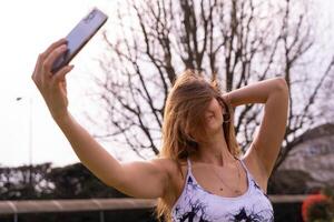 jung charmant blond sportlich Frau im Sportbekleidung posieren nehmen ein Selfie draußen foto