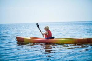 Frau mit Sicherheitsweste, die allein auf einer ruhigen See Kajak fährt foto