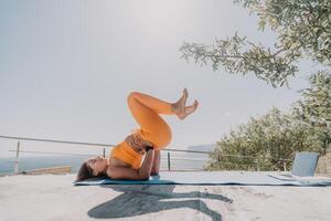 Fitness Frau Meer. glücklich Mitte alt Frau im Orange Sportbekleidung Übungen Morgen draußen auf Yoga Matte mit Laptop im Park Über Ozean Strand. weiblich Fitness Pilates Yoga Routine. gesund Lebensstil. foto