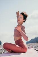 Mitte alt Gut suchen Frau mit schwarz Haar, Fitness Lehrer im Gamaschen und Spitzen tun Dehnen und Pilates auf Yoga Matte in der Nähe von das Meer. weiblich Fitness Yoga Routine Konzept. gesund Lebensstil foto