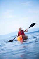 Frau mit Sicherheitsweste, die allein auf einer ruhigen See Kajak fährt foto