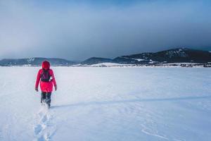 Frau, die an einem kalten Wintertag einsam auf einem zugefrorenen See spaziert foto