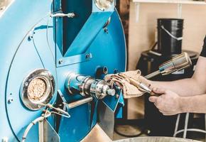 Erntearbeiter, der Bohnen im Kaffeeröster überprüft foto