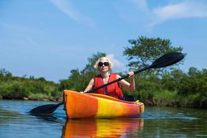 Frau mit Warnweste, die alleine auf einem ruhigen Fluss Kajak fährt foto