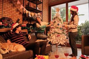 Familie mit Hund und Freunden schmücken glücklich den weißen Weihnachtsbaum im Wohnzimmer des Hauses, bereiten sich lustig und fröhlich auf eine Feier zum Neujahrsfest vor.