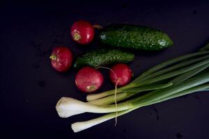 das zuerst Frühling Gemüse auf ein schwarz Hintergrund, Grün Zwiebel, Rettich, Gurke foto