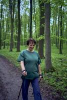Alten Frau ist beschäftigt, verlobt im nordisch Gehen mit Stöcke im das Frühling Wald foto