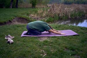 alt Frau Praktiken Methoden Ausübungen Yoga im das Morgen auf das Fluss Bank, kam von Zuhause durch Fahrrad foto