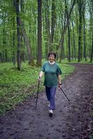 Alten Frau ist beschäftigt, verlobt im nordisch Gehen mit Stöcke im das Frühling Wald foto