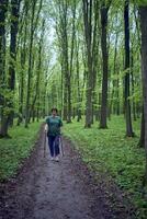 Alten Frau ist beschäftigt, verlobt im nordisch Gehen mit Stöcke im das Frühling Wald foto