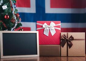 klein Tafel und Geschenk Kisten auf hölzern Tabelle mit ein Weihnachten Baum und Norwegen Flagge im das Hintergrund. Raum zum Text. Konzept von Weihnachten und Neu Jahr Festival foto