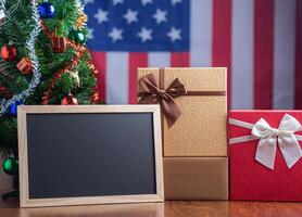 klein Tafel und Geschenk Kisten auf hölzern Tabelle mit ein Weihnachten Baum und amerikanisch Flagge im das Hintergrund. Raum zum Text. Konzept von Weihnachten und Neu Jahr Festival foto