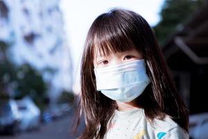Kopfschuss. süßes Mädchen, das eine medizinische Gesichtsmaske trägt, um den Ausbruch von Staub pm2.5 und Coronavirus im Freien zu verhindern. Kinder sitzen am Abend spielend. Kind ist 3-4 Jahre alt. foto