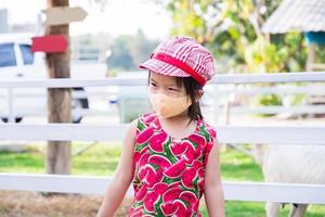 süßes asiatisches mädchen, das eine orange stoffgesichtsmaske trägt. Kind besucht Zoo während des Ausbruchs des Coronavirus. verhindern luftverschmutzung pm2.5 staub. Kind trägt rote Sonnenhaube passendes Kleid. Happy Kids ist 4 Jahre alt. foto