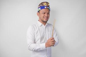 balinesisch Mann tragen traditionell Kopfschmuck namens udeng tun bezahlen Respekt Geste während halten beten Weihrauch auf isoliert Weiß Hintergrund foto