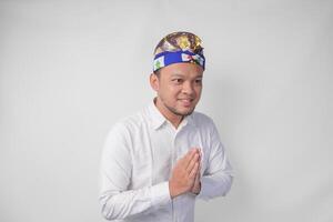 lächelnd jung balinesisch Mann tragen traditionell Kopfschmuck namens udeng tun Gruß oder herzlich willkommen Geste, isoliert Über Weiß Hintergrund foto