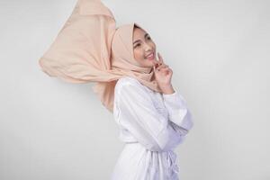 elegant jung asiatisch Muslim Frau tragen Weiß Kleid mit Hijab winken im das Wind, Modellieren Pose auf Weiß Hintergrund foto