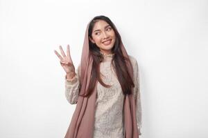 Porträt von attraktiv asiatisch Muslim Frau tragen Schleier Hijab geben Nummer einer zu zehn durch Hand Geste, Stehen Über isoliert Weiß Hintergrund foto