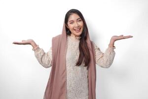 asiatisch Muslim Frau tragen Kopftuch Schleier Hijab lächelnd fröhlich während suchen und zeigen zu Kopieren Raum neben ihr, Stehen auf isoliert Weiß Hintergrund foto