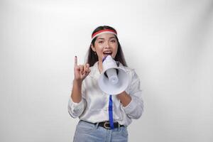 energisch indonesisch Frau im beiläufig formal Outfit tragen Land Flagge Stirnband während halten und schreien beim Megaphon, stolz zeigen wenig Finger eingetaucht im lila Tinte nach Wählen zum Wahl foto