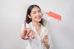 Porträt von glücklich asiatisch Frau stolz zeigen wenig Finger eingetaucht im lila Tinte nach Wählen zum Präsident und Parlament Wahl, links Hand halten Indonesien Mini Flaggen. Unabhängigkeit Tag Konzept. foto