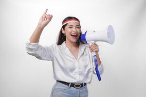 energisch indonesisch Frau im beiläufig formal Outfit tragen Land Flagge Stirnband während halten und schreien beim Megaphon, stolz zeigen wenig Finger eingetaucht im lila Tinte nach Wählen zum Wahl foto