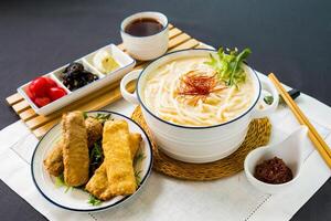 Fisch knusprig rollen Fisch Udon im Reich Fisch Suppe Nudel mit Chili Soße und Essstäbchen serviert im Schüssel isoliert auf Serviette Seite Aussicht von japanisch Essen auf Tabelle foto