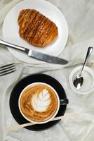 heiß Macchiato Kaffee Latté Kunst serviert im Tasse mit Croissant, Puff Gebäck, Brot und Messer isoliert auf Serviette oben Aussicht Cafe Frühstück foto