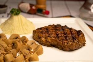 Unterschrift gegrillt Rippe Auge Rindfleisch Steak mit Pilz, tauchen, schwarz Pfeffer und Knoblauch Chili Soße serviert im Gericht isoliert auf Serviette Seite Aussicht auf hölzern Tabelle Italienisch Essen foto