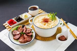 Spanisch geräuchert iberico Schweinefleisch Fisch Udon im Reich Fisch Suppe mit Chili Soße und Essstäbchen serviert im Schüssel isoliert auf Serviette Seite Aussicht von japanisch Essen auf Tabelle foto