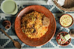 Hammelfleisch kacchi Biryani mit Salat, borhani und Chui Pitha serviert im Gericht isoliert auf Matte oben Aussicht von indisch und Bangladesch Essen foto