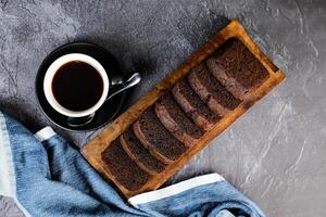 Schokolade Kuchen Scheibe serviert auf hölzern Tafel mit Tasse von schwarz Kaffee isoliert auf Serviette oben Aussicht von Französisch Frühstück gebacken Essen Artikel auf grau Hintergrund foto