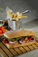 Ciabatta geräuchert Schinken Sandwich isoliert auf hölzern mit Mayonnaise tauchen und Französisch Fritten Eimer Tafel Seite Aussicht von Italienisch schnell Essen auf grau Hintergrund foto