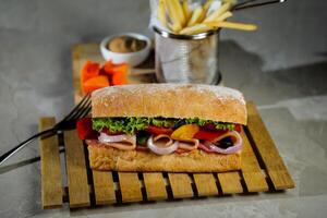 Ciabatta geräuchert Schinken Sandwich isoliert auf hölzern mit Mayonnaise tauchen und Französisch Fritten Eimer Tafel Seite Aussicht von Italienisch schnell Essen auf grau Hintergrund foto