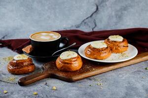 Zimt rollen serviert auf hölzern Tafel mit Tasse von Kaffee Latté Kunst isoliert auf Serviette Seite Aussicht von Französisch Frühstück gebacken Essen Artikel foto
