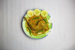 Bangladesch Hähnchen braten Bein mit Bratensoße, Koriander, Gurke und Grün Chili serviert im Teller isoliert auf Hintergrund oben Aussicht von bangladesch, indisch und pakistanisch traditionell würzig Essen foto