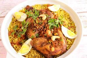 räumlich Hähnchen quzi oder ghozi kabsa mandi Reis pulao mit gebraten Zwiebel, Cashew Nuss und gekocht Ei serviert im Topf Gericht isoliert auf hölzern Tabelle oben Aussicht Arabisch würzig Essen foto