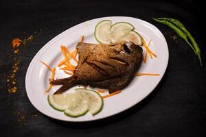 gebraten Pomfret Fisch oder Abonnieren braten mit Limette Scheibe serviert im Gericht isoliert auf dunkel Hintergrund oben Aussicht indisch Gewürze, Bangladesch und pakistanisch Essen foto