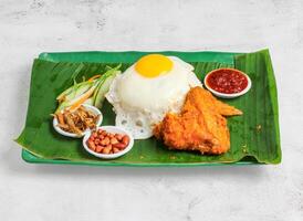 nasi Lemak einstellen mit sonnig Ei, Reis, Hähnchen Flügel, Essiggurke, Salat, Erdnuss und Chili Soße serviert im Gericht isoliert auf Banane Blatt oben Aussicht von Singapur Essen foto