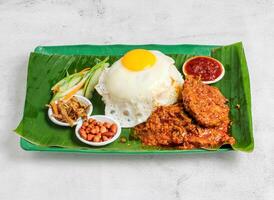 nasi Lemak einstellen mit sonnig Ei, Reis, Hähnchen hacken, Essiggurke, Salat, Erdnuss und Chili Soße serviert im Gericht isoliert auf Banane Blatt oben Aussicht von Singapur Essen foto