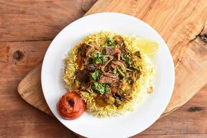 würzig Lamm Biryani Reis pulao mit Tomate, gebraten Zwiebel und Limette serviert im Gericht isoliert auf hölzern Tabelle oben Aussicht Mitte östlichen Mittagessen Essen foto