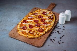 Peperoni Pizza mit schwarz Pfeffer Portion auf hölzern Schneiden Tafel isoliert auf grau Hintergrund oben Aussicht von Fast Food foto