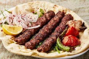 Arabisch Fleisch Kabab mit Safran, Zwiebel, Tomate, Pita-Brot brot, Zitrone Scheibe und Salat serviert im Gericht isoliert auf Tabelle oben Aussicht von Arabisch Essen foto